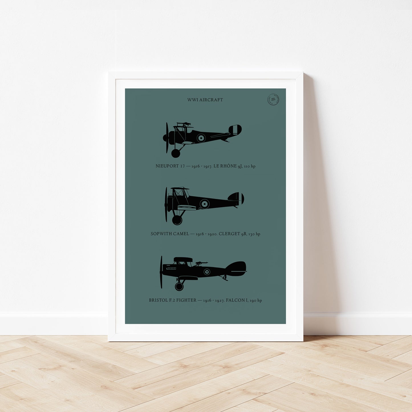 Framed poster standing on wood flooring, leaning against a white wall. It shows the profiles of three WW1 period aeroplanes in a black silhouette style over a dark green background