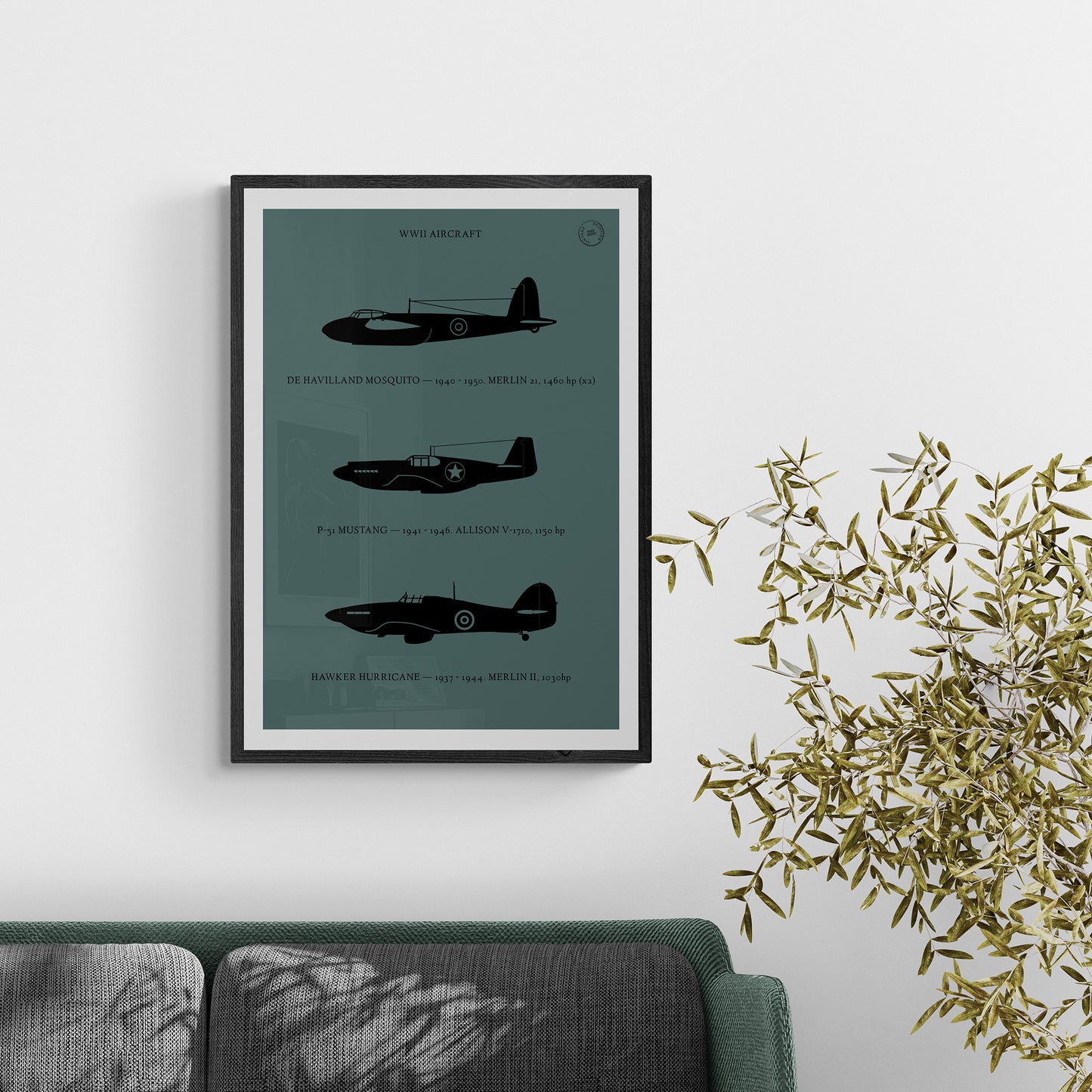 A framed poster hanging over a green and grey sofa next to a plant. It shows the profiles of three WW1 period aeroplanes in a black silhouette style over a dark green background