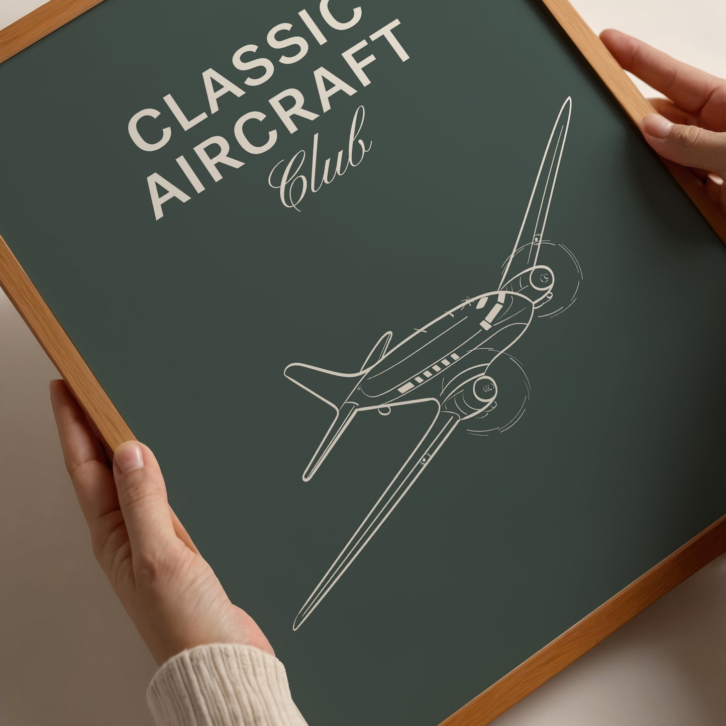 Closeup of a famed poster being held by a person. It shows a white illustration of a vintage aircraft in a dark green background with the words Classic Aircraft Club