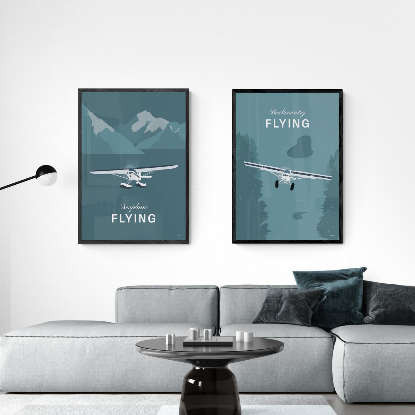 Two framed prints hanging in a modern living room over a light grey sofa. The first shows a light aircraft illustration with the words seaplane flying. The second shows a light aircraft illustration with the words backcountry flying. Both in white over a teal