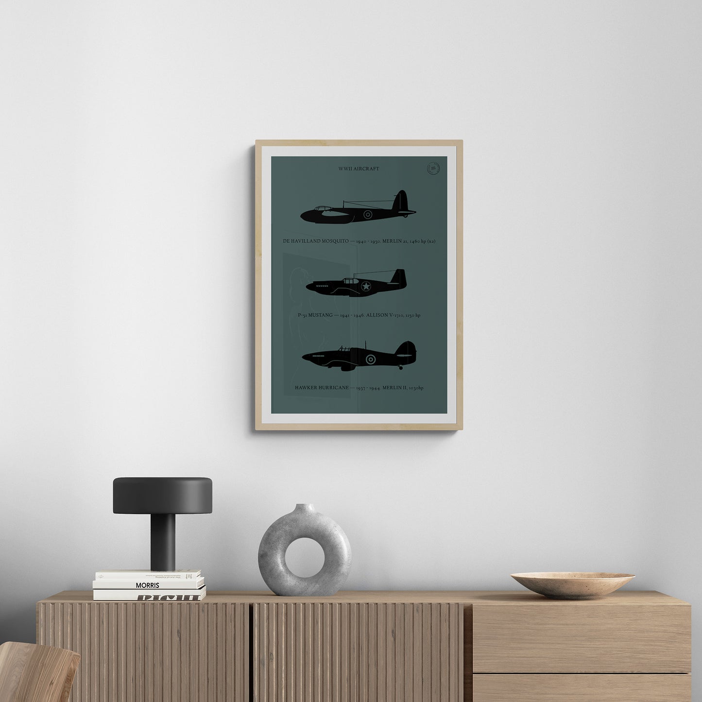 A framed poster hanging over a wooden cabinet in a modern looking room. It shows the profiles of three WW1 period aeroplanes in a black silhouette style over a dark green background