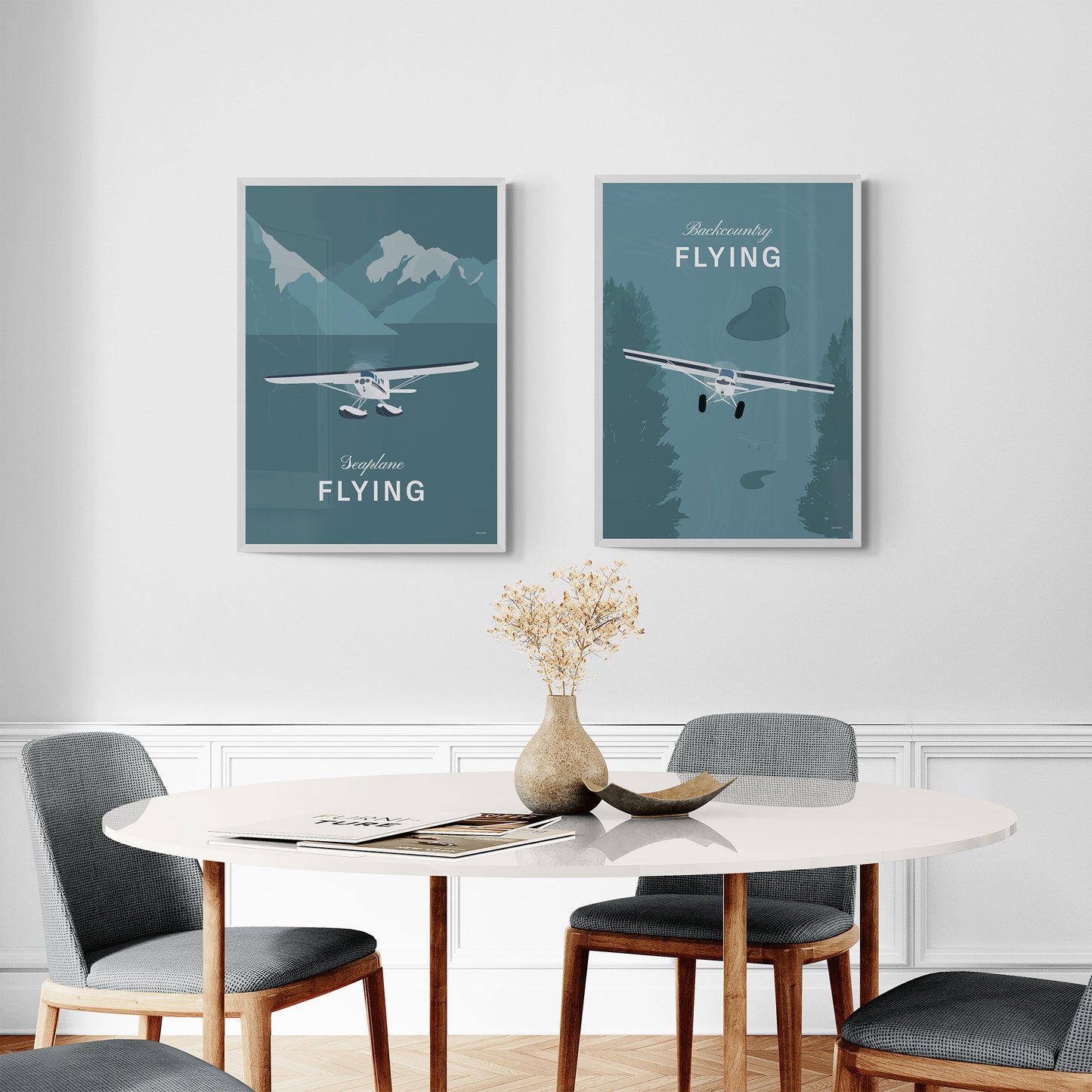 A pair of framed prints hanging in a modern dining room over a circular table and chairs. The first shows a light aircraft illustration with the words seaplane flying. The second shows a light aircraft illustration with the words backcountry flying. Both in white over a teal