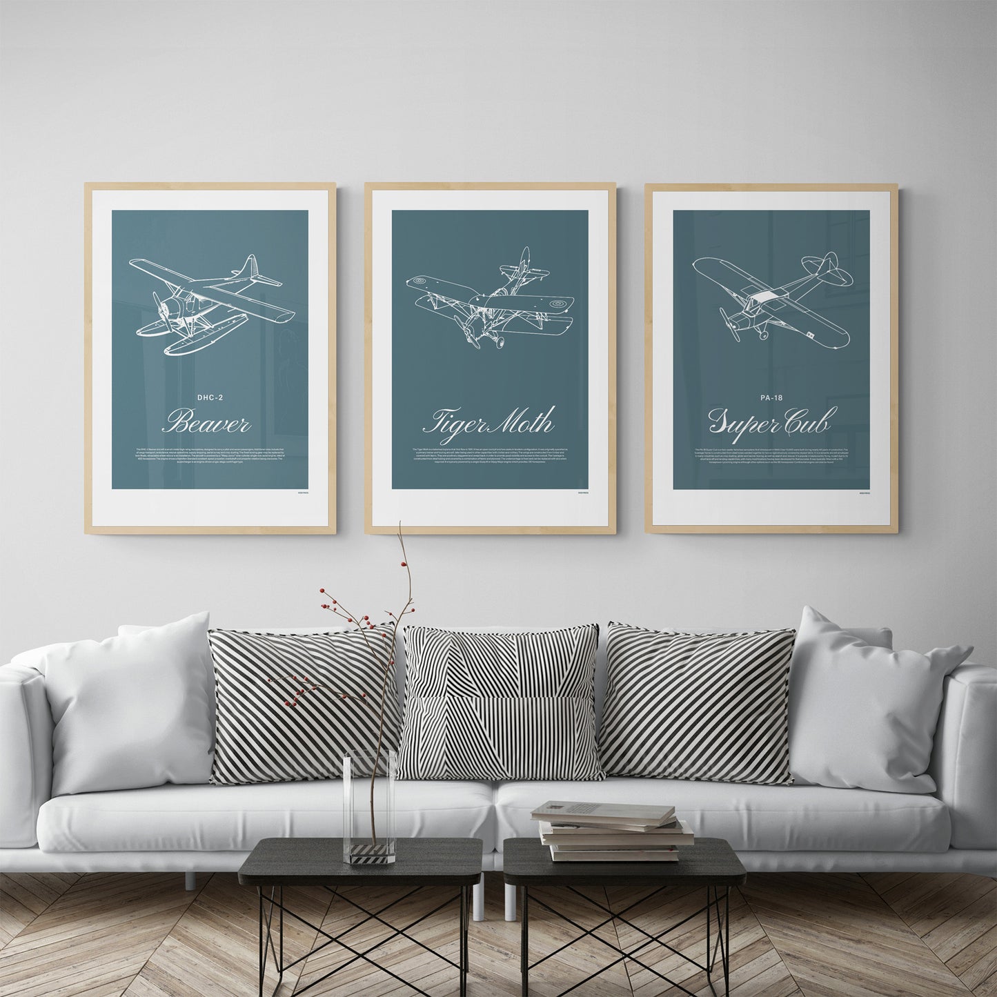 Three framed posters hanging in a modern brightly lit living room over a grey sofa with cushions. Each shows a white illustration on a teal background of a light aircraft - DHC-2 Beaver, Tiger Moth, PA-18 Super Cub