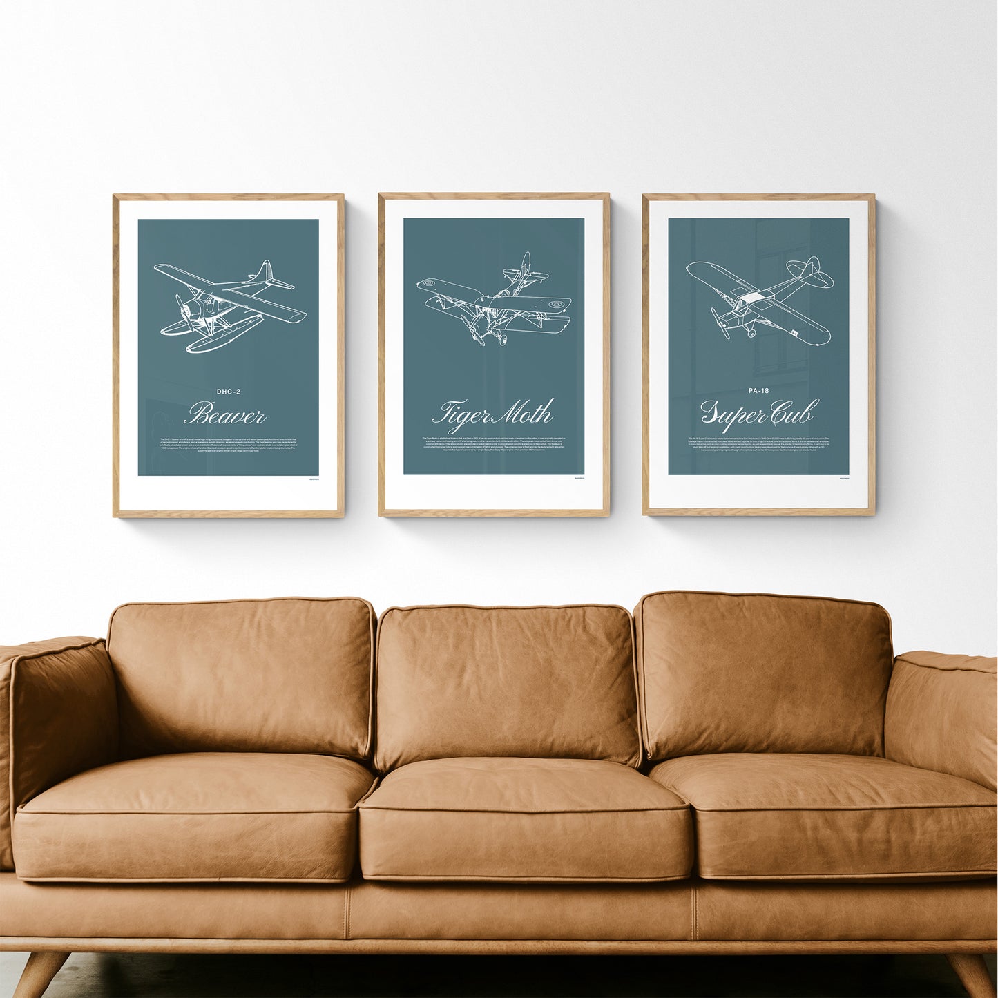Three framed posters hanging over a leather sofa. Each shows a white illustration on a teal background of a light aircraft - DHC-2 Beaver, Tiger Moth, PA-18 Super Cub
