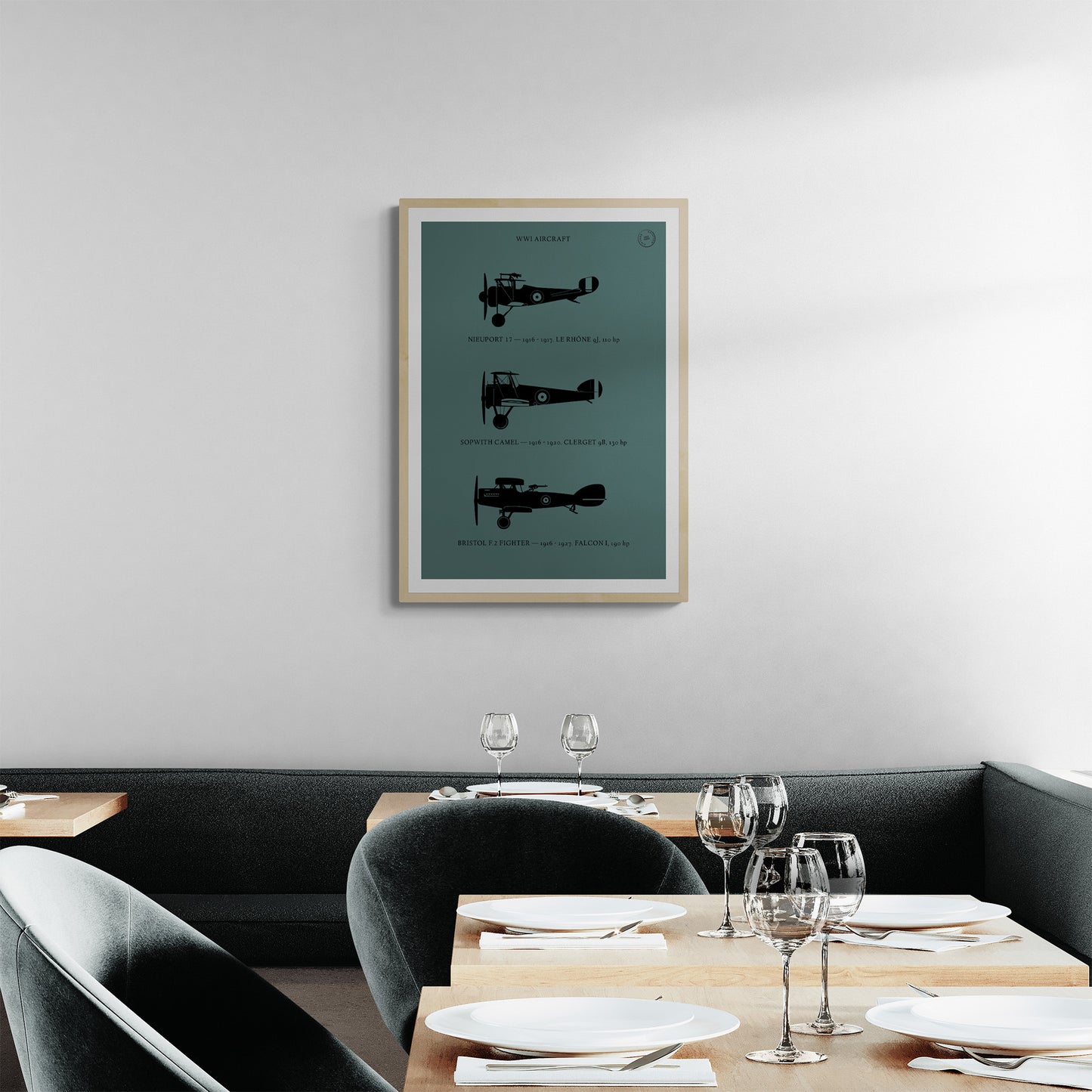 A framed print hanging in a modern looking restaurant scene. It shows the profiles of three WW1 period aeroplanes in a black silhouette style over a dark green background