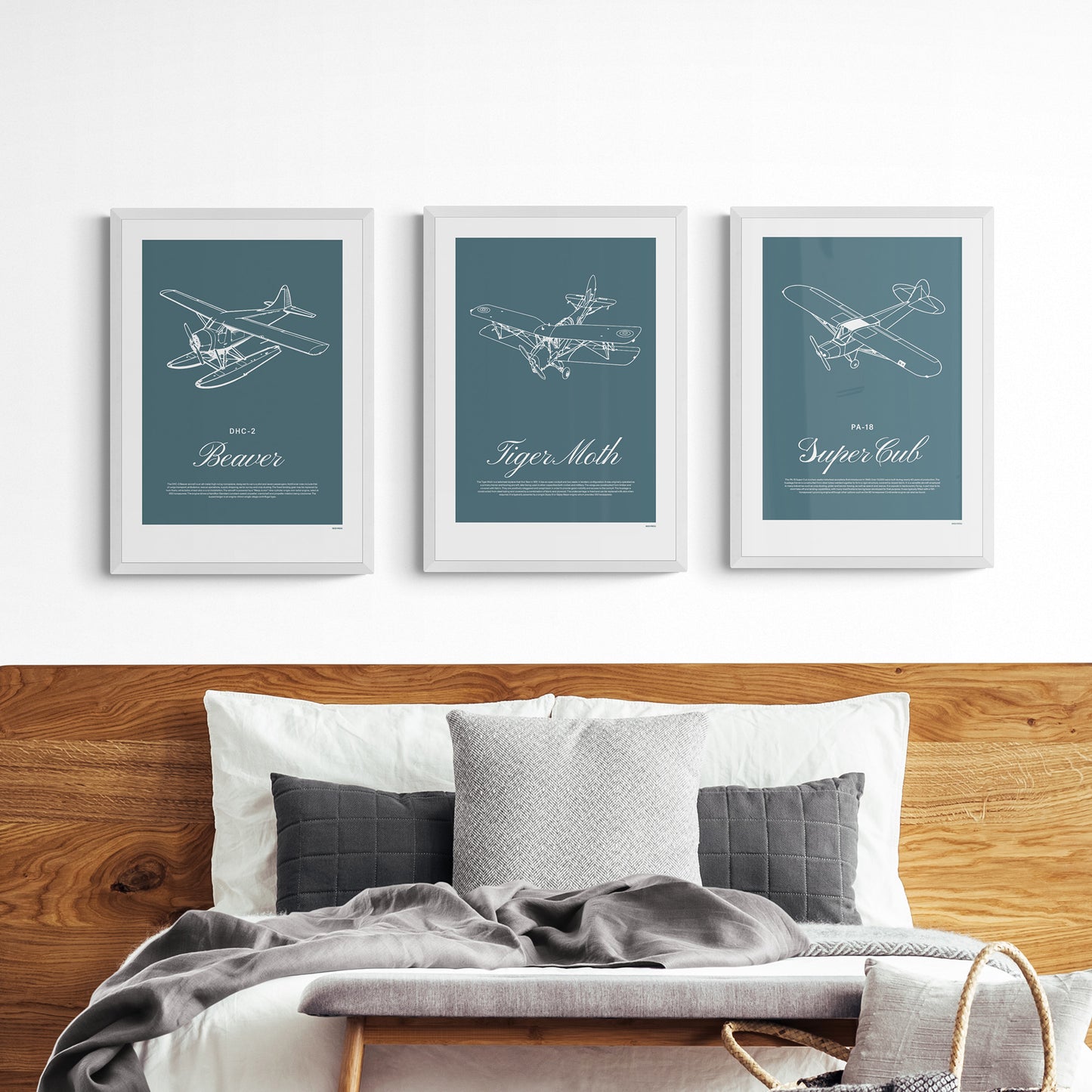 Three framed posters hanging in a living room over a bed with a wooden head board, cushions pillows and throws. Each shows a white illustration on a teal background of a light aircraft - DHC-2 Beaver, Tiger Moth, PA-18 Super Cub