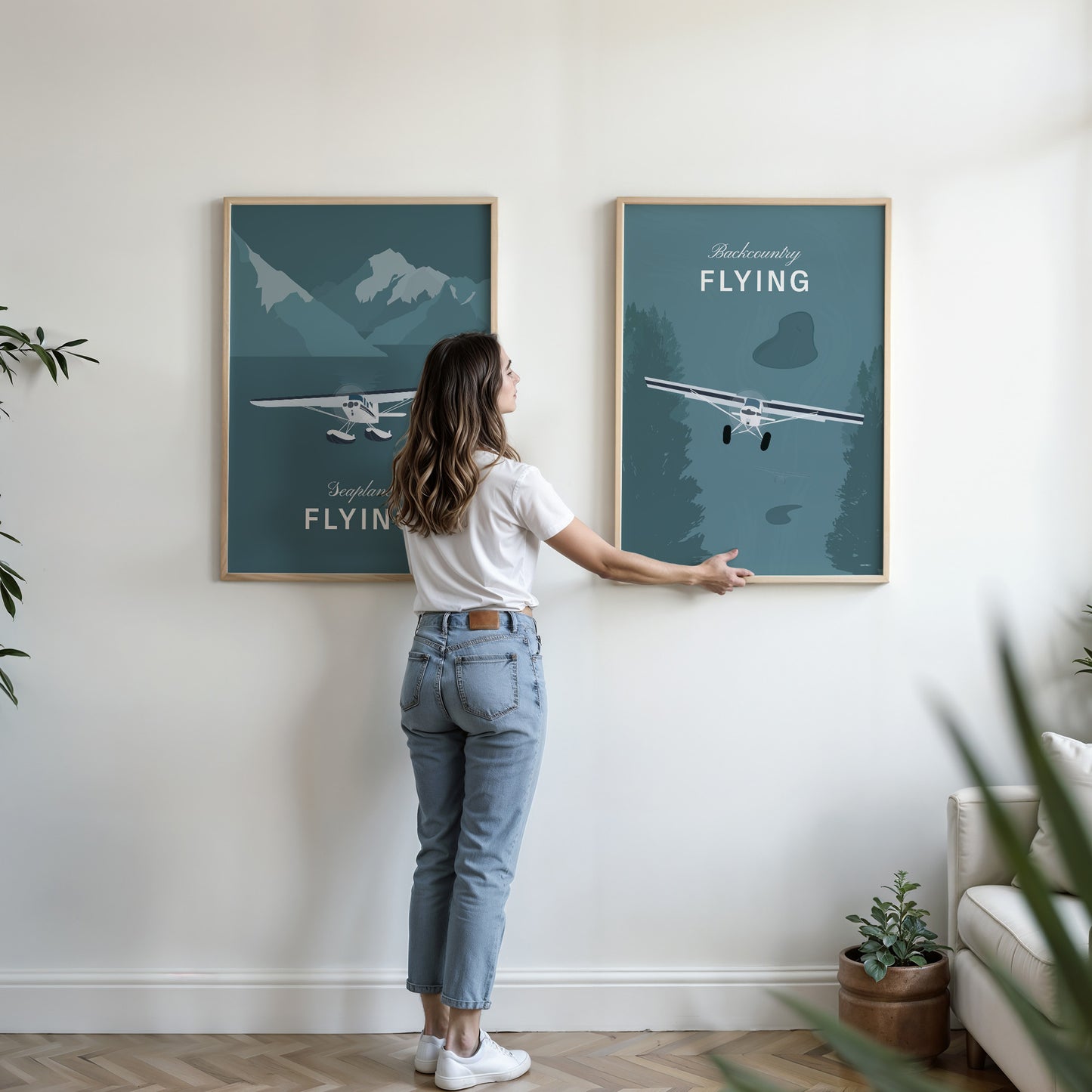 A woman hanging two framed prints in the living room the first shows a light aircraft illustration with the words seaplane flying the second shows a light aircraft illustration with the words backcountry flying