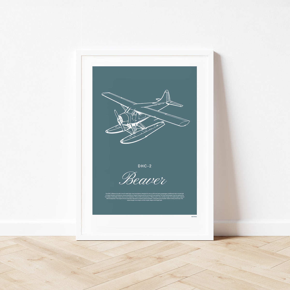 Framed poster standing on wood flooring, leaning against a white wall. It shows a light aircraft illustration with the words DHC-2 Beaver in white over a teal background