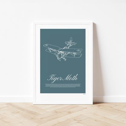 Framed poster standing on wood flooring, leaning against a white wall. It shows a light aircraft illustration with the words Tiger Moth in white over a teal background