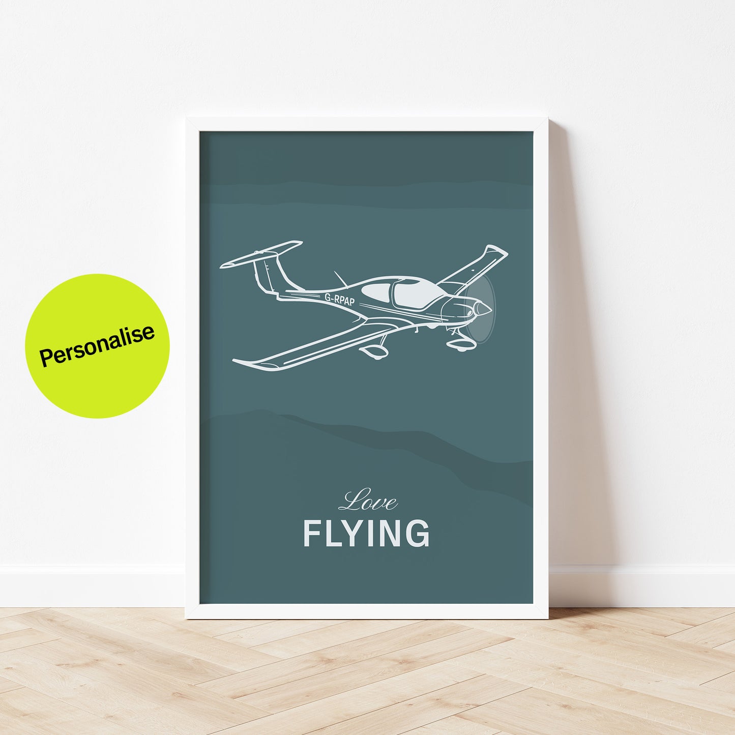 Framed poster standing on wood flooring, leaning against a white wall. It shows a light aircraft illustration with the words Love Flying in white over a teal background. On top of the image the words personalise are visible 