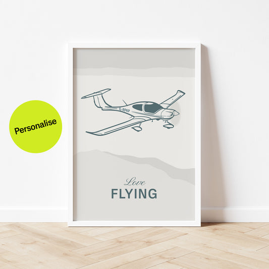 Framed poster standing on wood flooring, leaning against a white wall. It shows a light aircraft illustration with the words Love Flying in white over an off white background