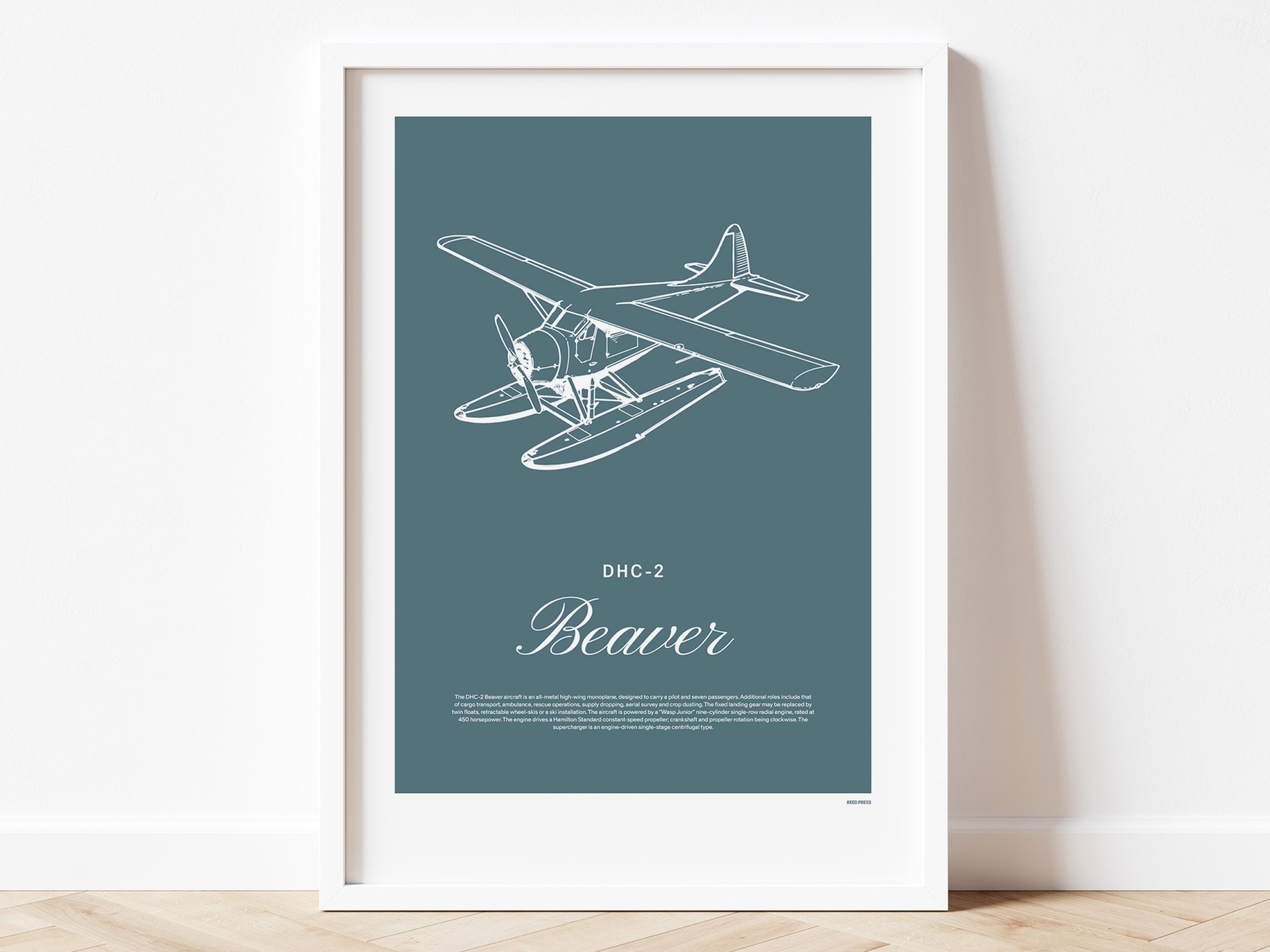 Framed poster standing on wood flooring, leaning against a white wall. It shows a light aircraft illustration with the words DHC-2 Beaver in white over a teal background