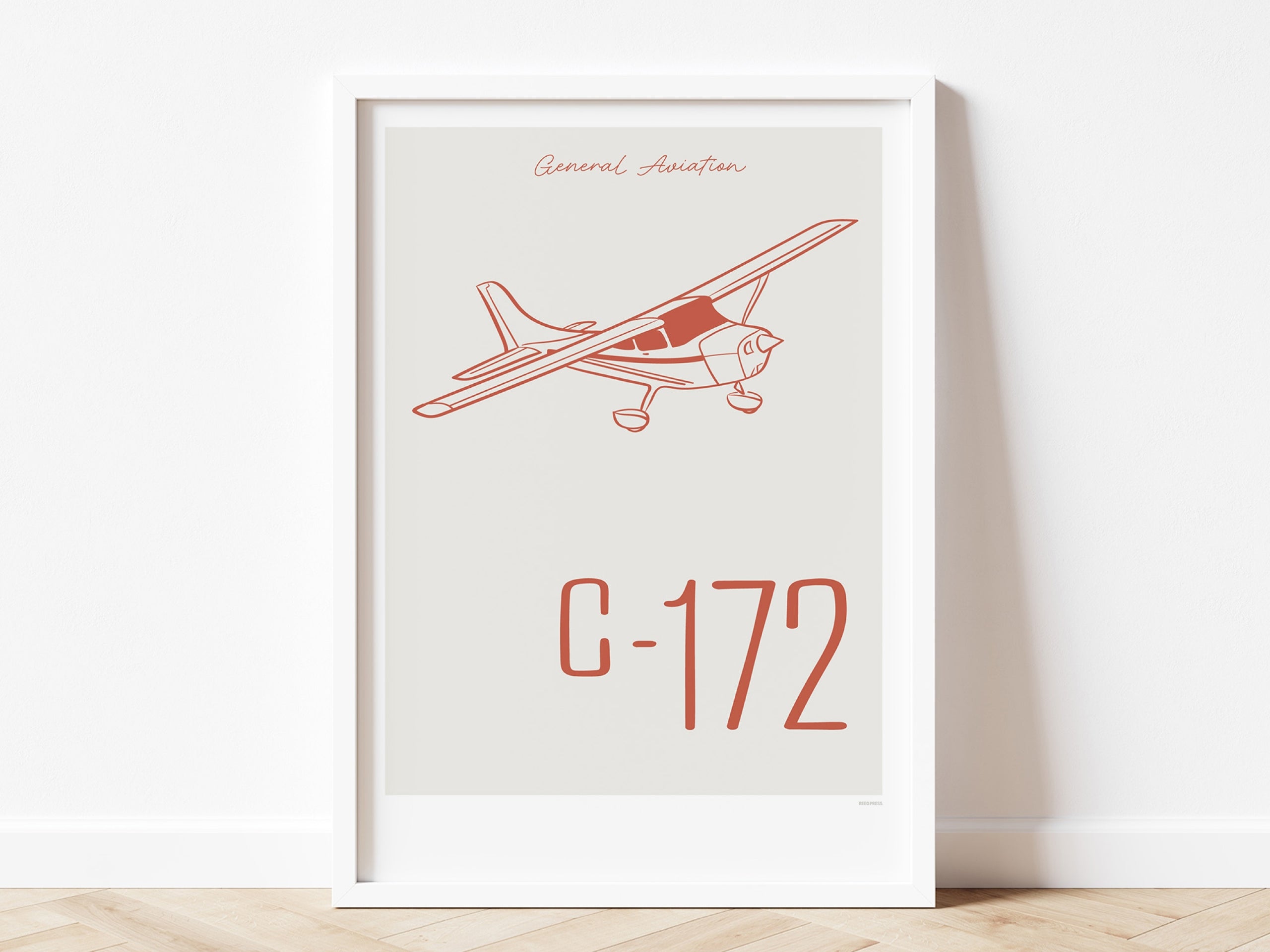 Framed poster standing on wood flooring, leaning against a white wall. It shows a light aircraft illustration with the words General Aviation and C-172 in red