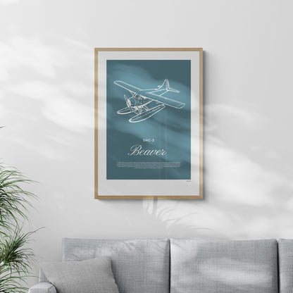 A framed print hanging in a living room, over a grey sofa. It shows a light aircraft illustration with the words DHC-2 Beaver in white over a teal background