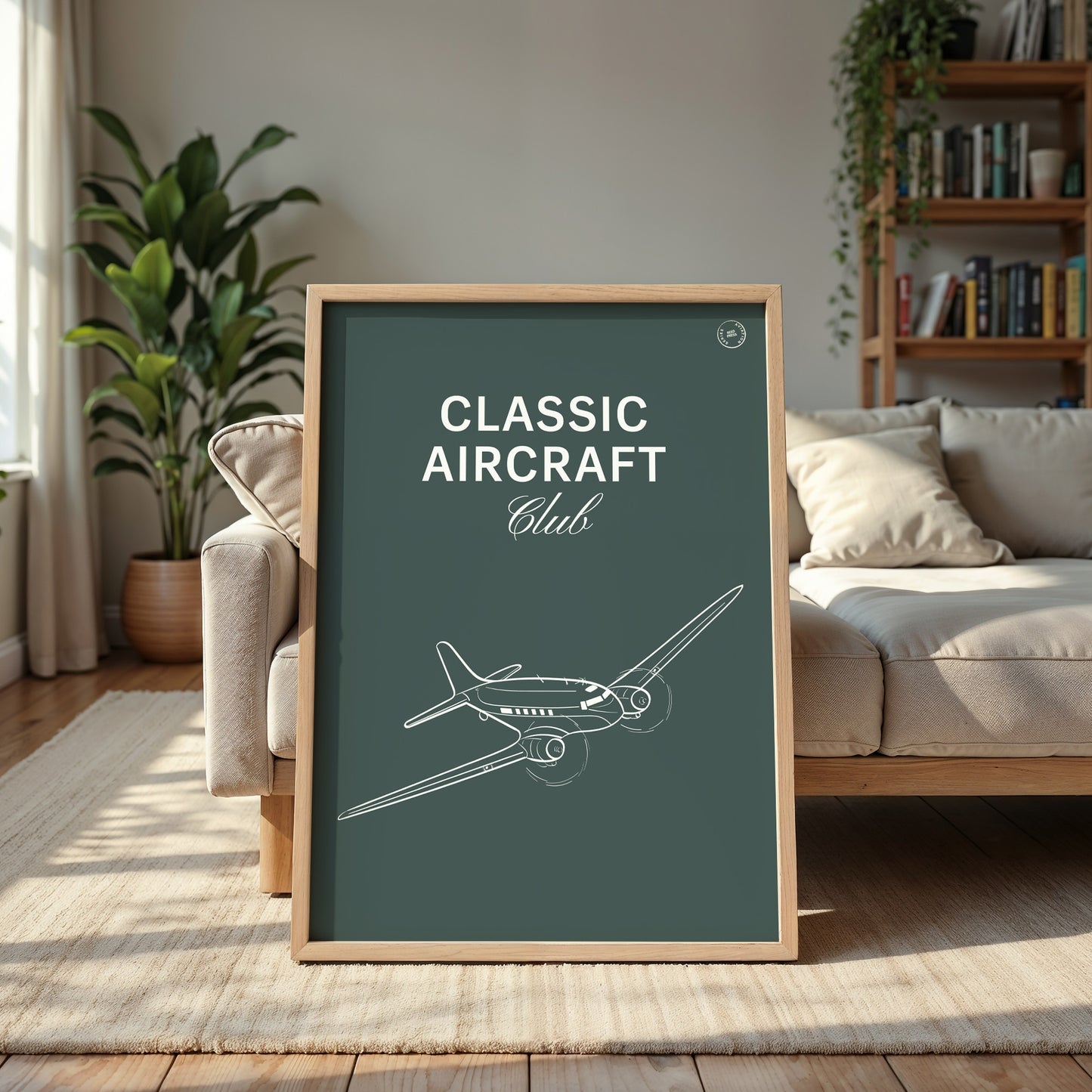 A living room with a a large framed poster leaning on a grey sofa. The poster shows a white illustration of a vintage aircraft in a dark green background with the words Classic Aircraft Club