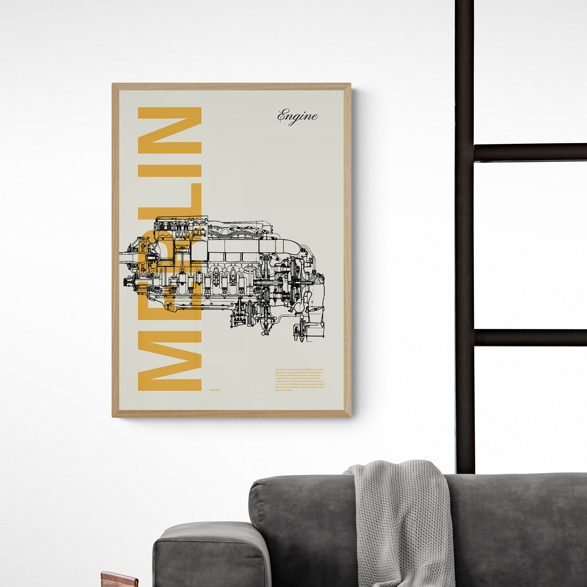 Close-up of a framed poster hanging over a dark grey sofa. It shows a Merlin aircraft engine in line drawing style with the word Merlin written big in mustard yellow