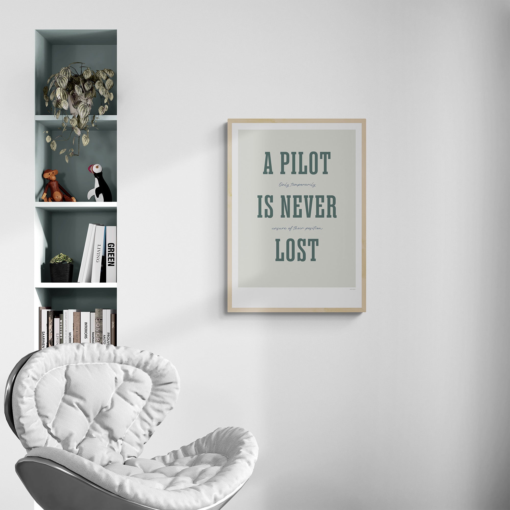 A framed print hanging in a modern home next to a bookshelf over a chair. It shows the words - A Pilot Is Never Lost - in large green letters and the words - Only temporarily unsure of their position - in in black handwritten style