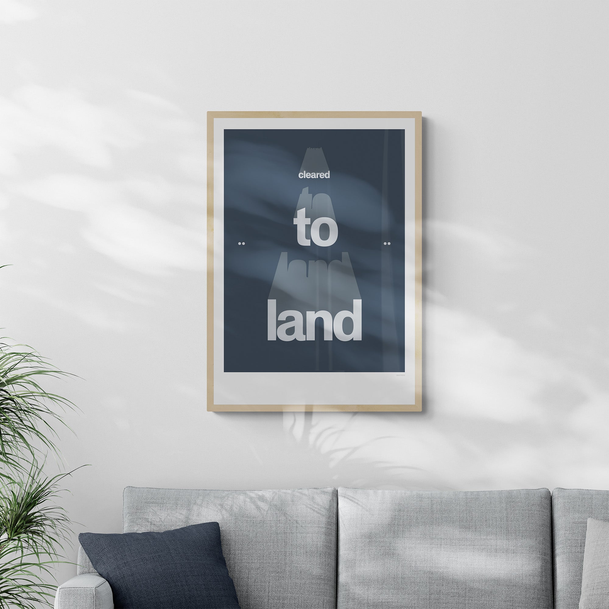 Framed poster hanging on a living room over a grey sofa. It shows the words cleared to land in white with a dark blue background 