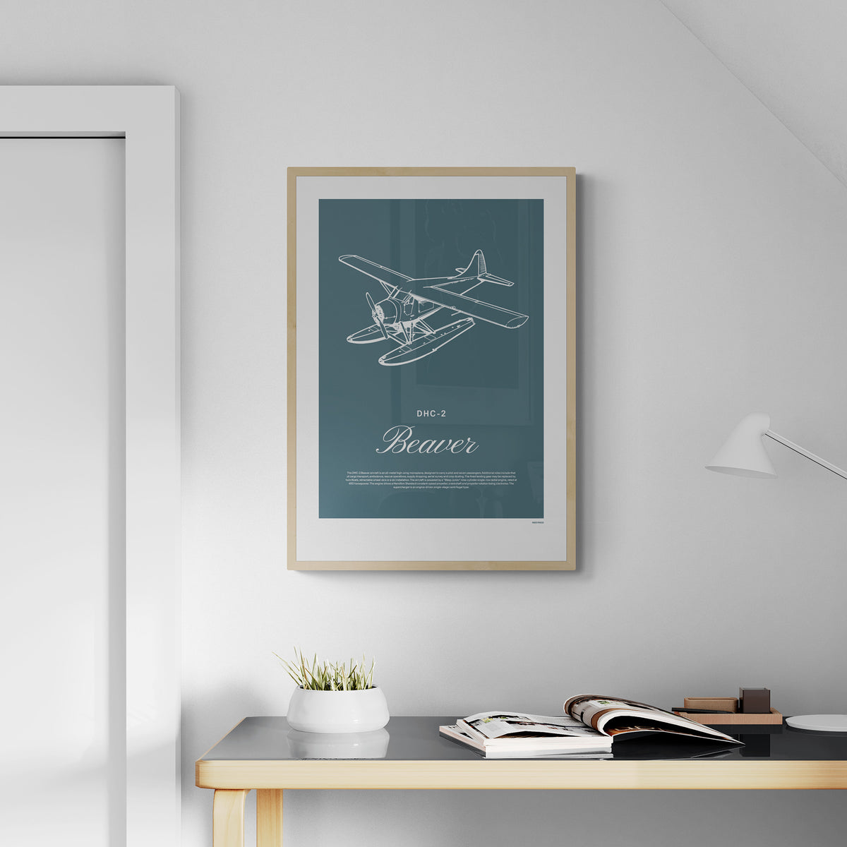 A framed print hanging in a home office, over a desk. It shows a light aircraft illustration with the words DHC-2 Beaver in white over a teal background