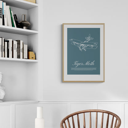 A framed poster hanging next to a bookshelf, and over a chair. It shows a light aircraft illustration with the words Tiger Moth in white over a teal background