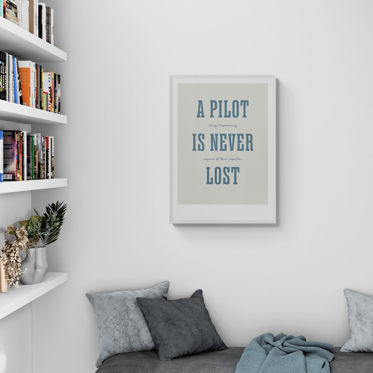 A framed print hanging in a home library over a beach seat. It shows the words - A Pilot Is Never Lost - in large blue letters and the words - Only temporarily unsure of their position - in in black handwritten style