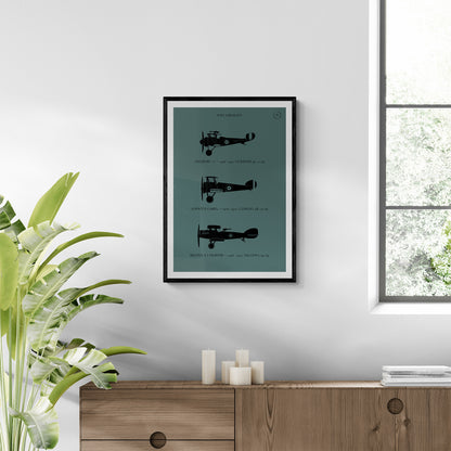 A framed print hanging in a modern brightly lit room over a wooden console table and next to a plant. It shows the profiles of three WW1 period aeroplanes in a black silhouette style over a dark green background 