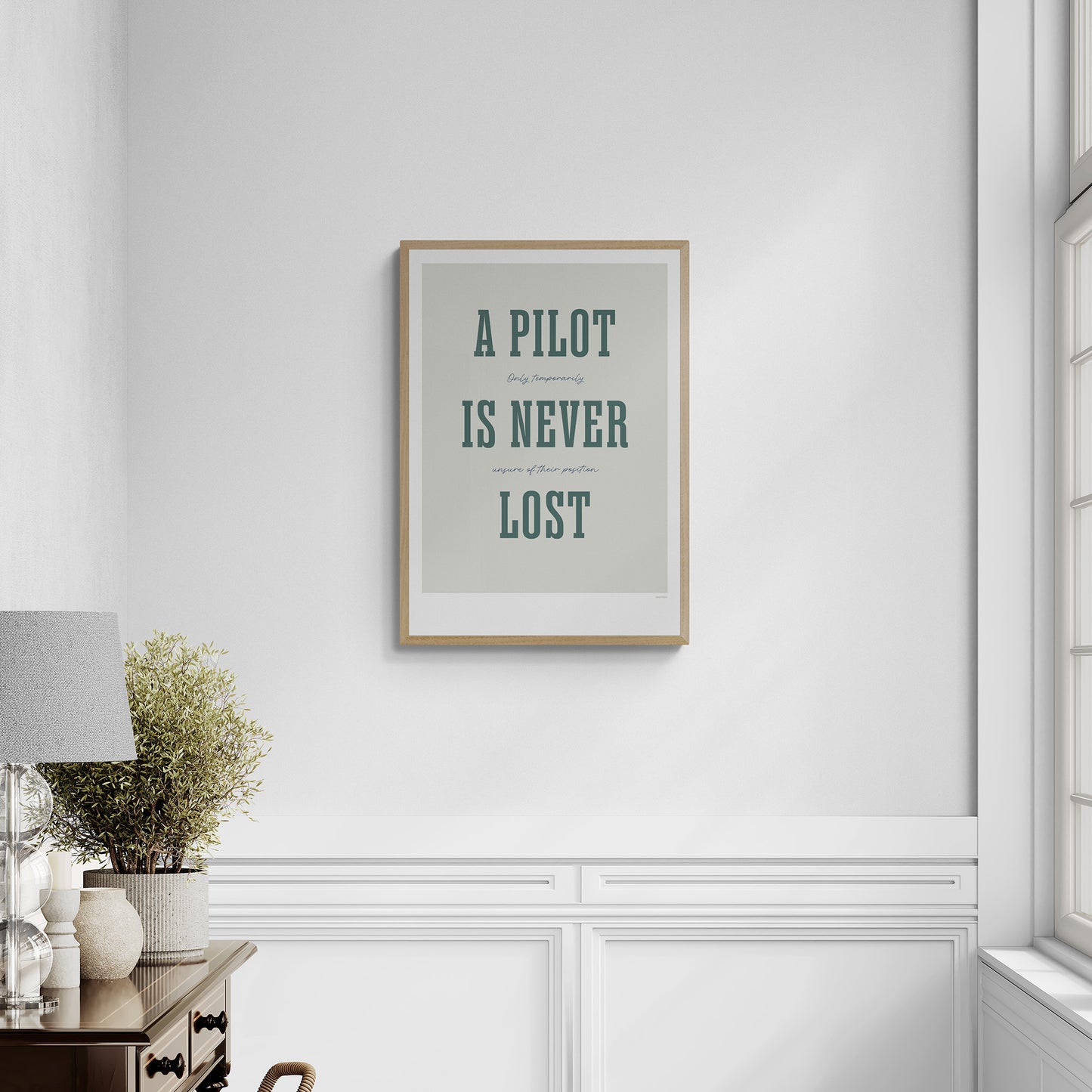 A framed print hanging in a luxurious home corridor. It shows the words - A Pilot Is Never Lost - in large green letters and the words - Only temporarily unsure of their position - in in black handwritten style