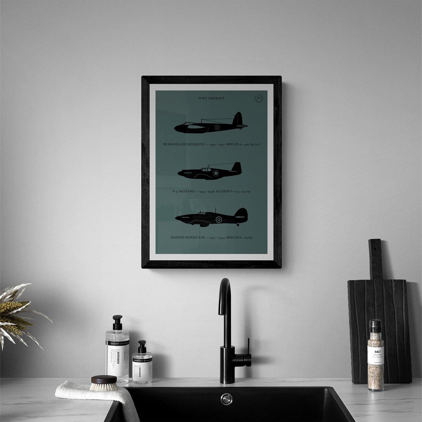 A framed poster hanging in a modern looking bathroom over a sink. I shows the profiles of three WW1 period aeroplanes in a black silhouette style over a dark green background 