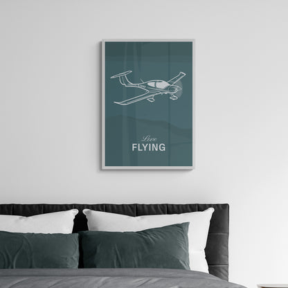 A framed print hanging over a bed with cushions. It shows a light aircraft illustration with the words Love Flying in white over a teal background