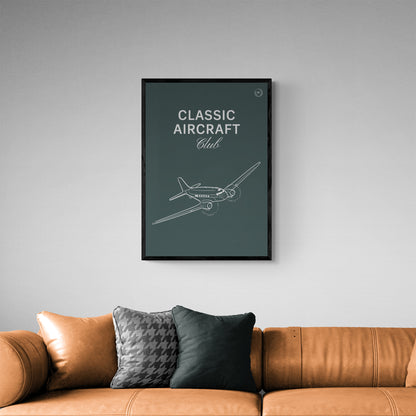 A framed poster hanging over a leather sofa. It shows a white illustration of a vintage aircraft in a dark green background with the words Classic Aircraft Club