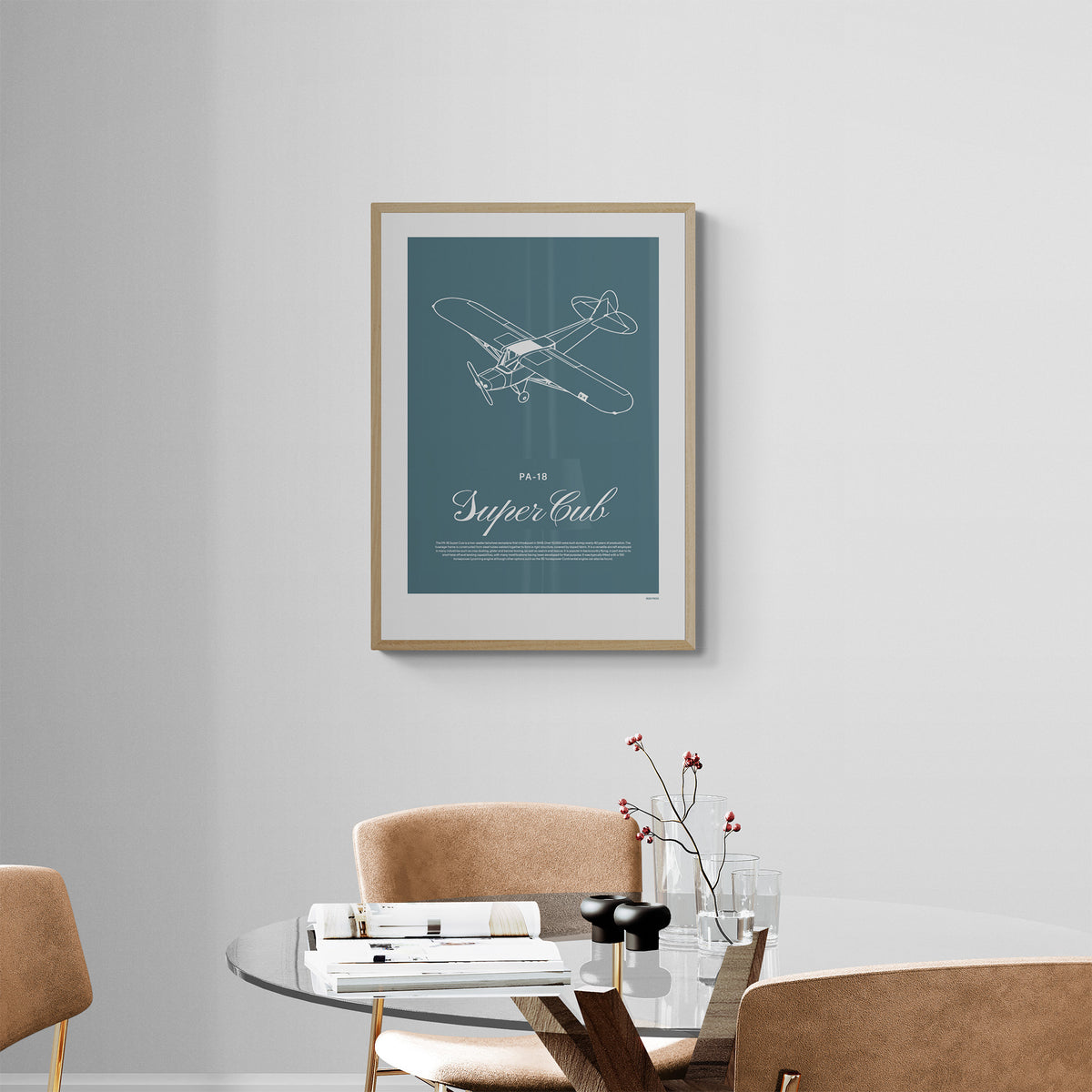 A framed print hanging on a modern dinning room over a table and chairs. It shows a light aircraft illustration with the words PA-18 Super Cub in white over a teal background