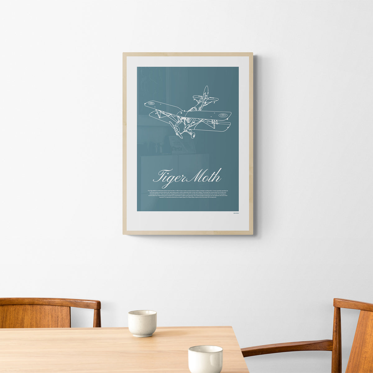 A framed poster hanging over a table and chairs. It shows a light aircraft illustration with the words Tiger Moth in white over a teal background