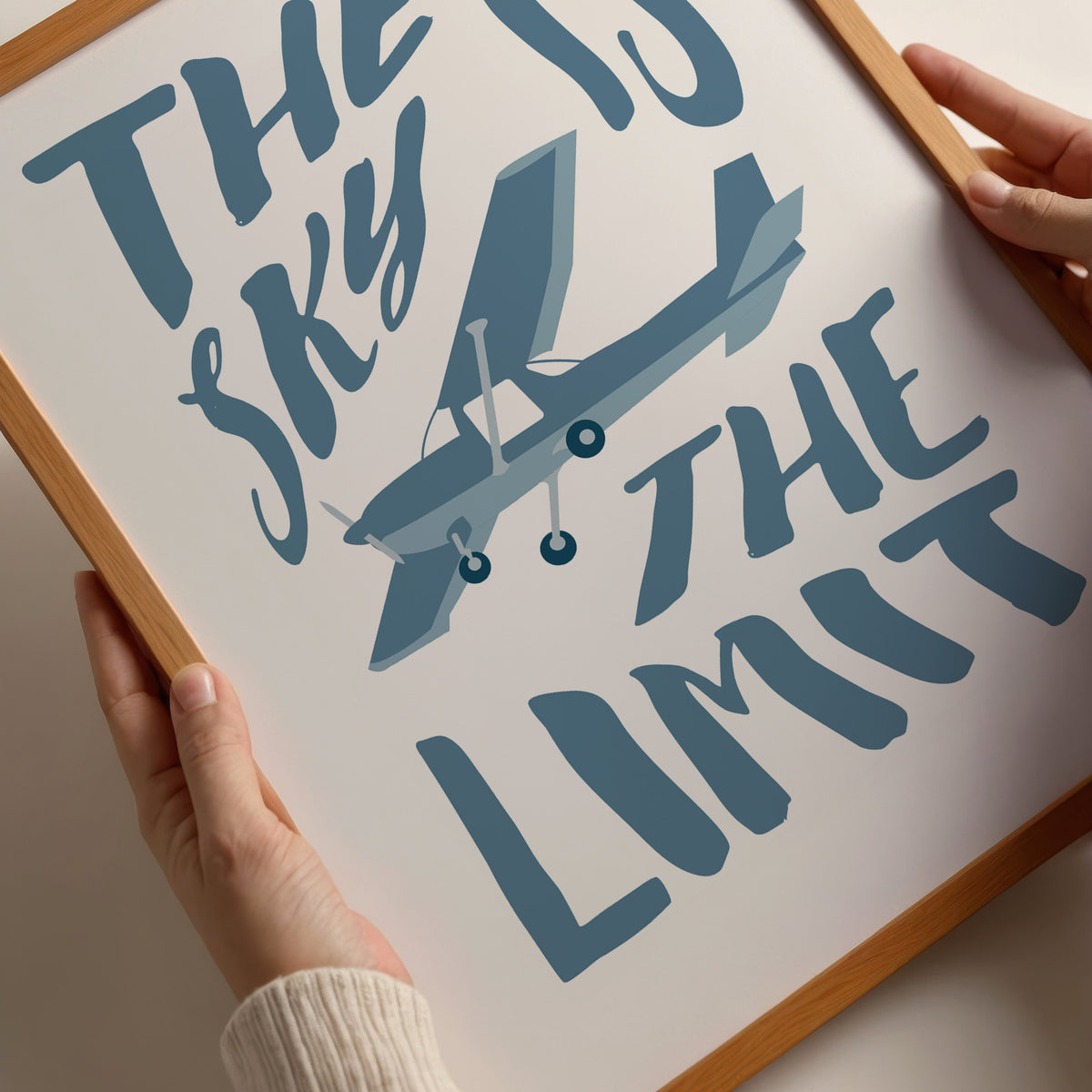 Closeup of a famed poster being held by a person. It shows an illustration of a light aircraft with the words THE SKY IS THE LIMIT composed around it in blue