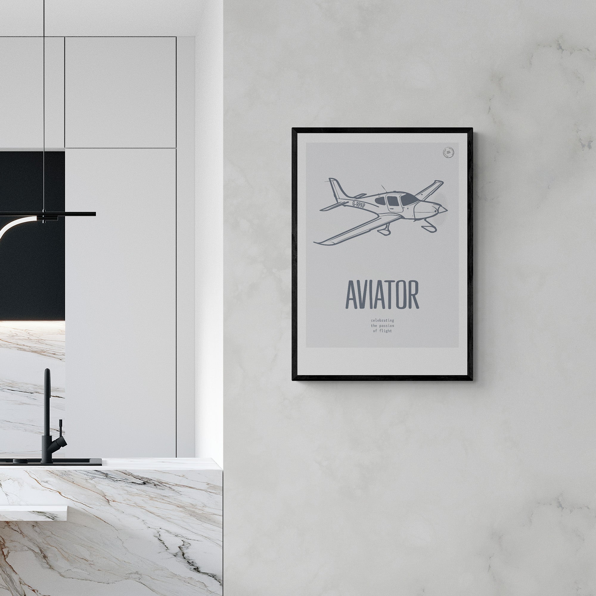 A framed print hanging in a modern kitchen on a marble wall. It shows a light aircraft illustration in white over a grey background with the word Aviator in large white letters