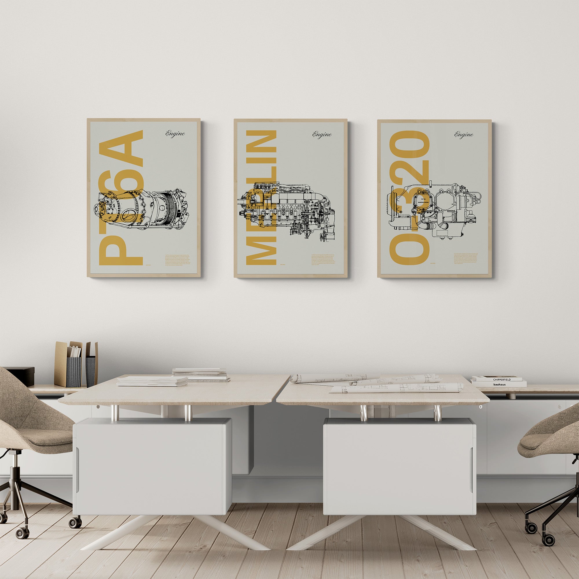 Three framed posters hanging in an office over two desks and chairs. Each shows a famous aircraft engines in line drawing style, with the engine name written big in mustard yellow