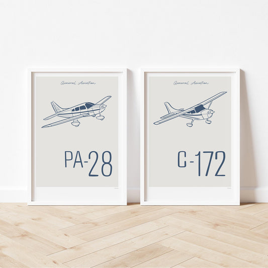 2 framed posters standing on wood flooring, leaning against a white wall. Each shows a light aircraft illustration with the words General Aviation and the aircraft name in blue